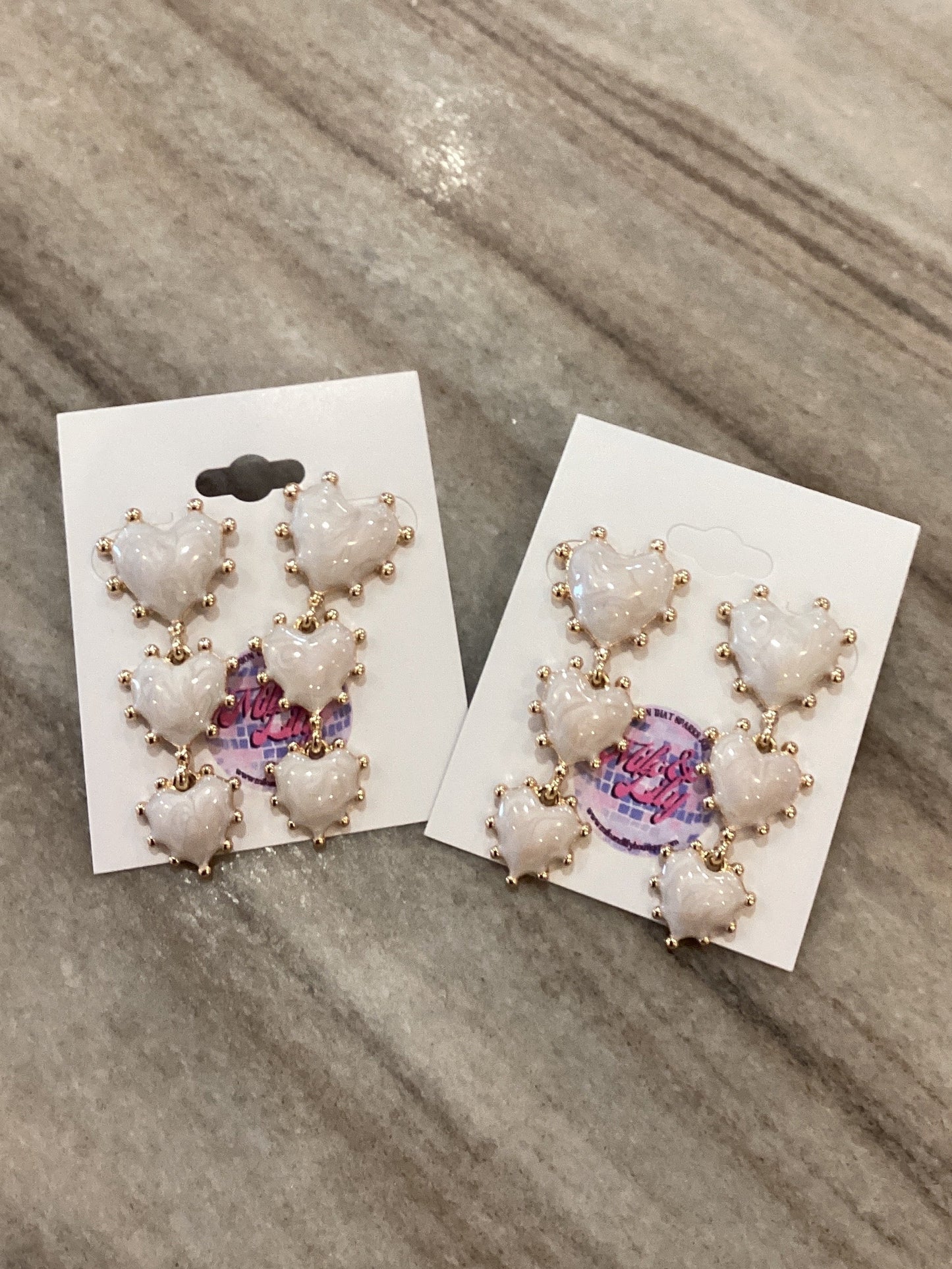 White heart stud earrings with gold accents on display cards, on a marble surface
