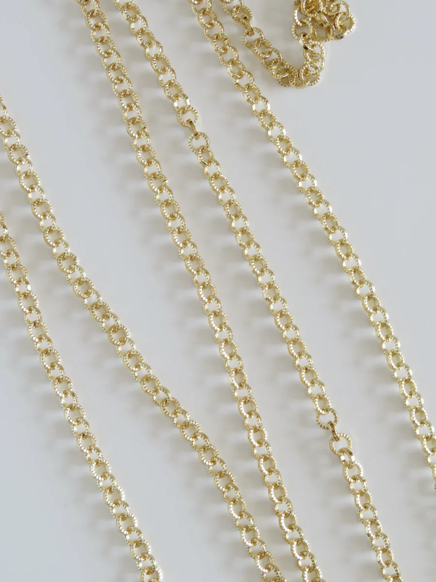 Close up of delicate gold chain necklaces, shiny textured links on a light background