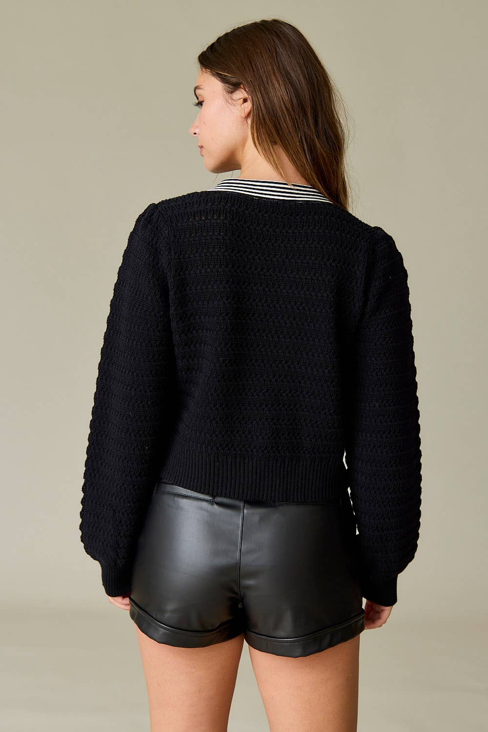 Back view of Black textured knit sweater with two black-and-white striped statement bows on the front and a deep V-neckline, styled with black leather shorts