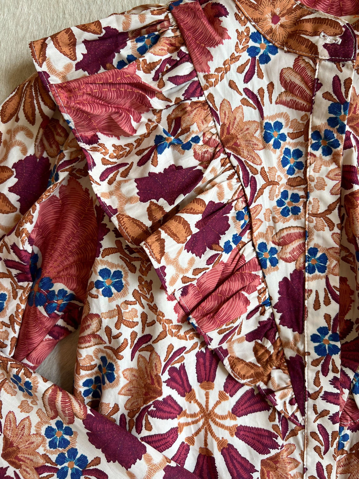 Women's blouse with ruffled collar and vibrant floral pattern in red, brown, and blue.