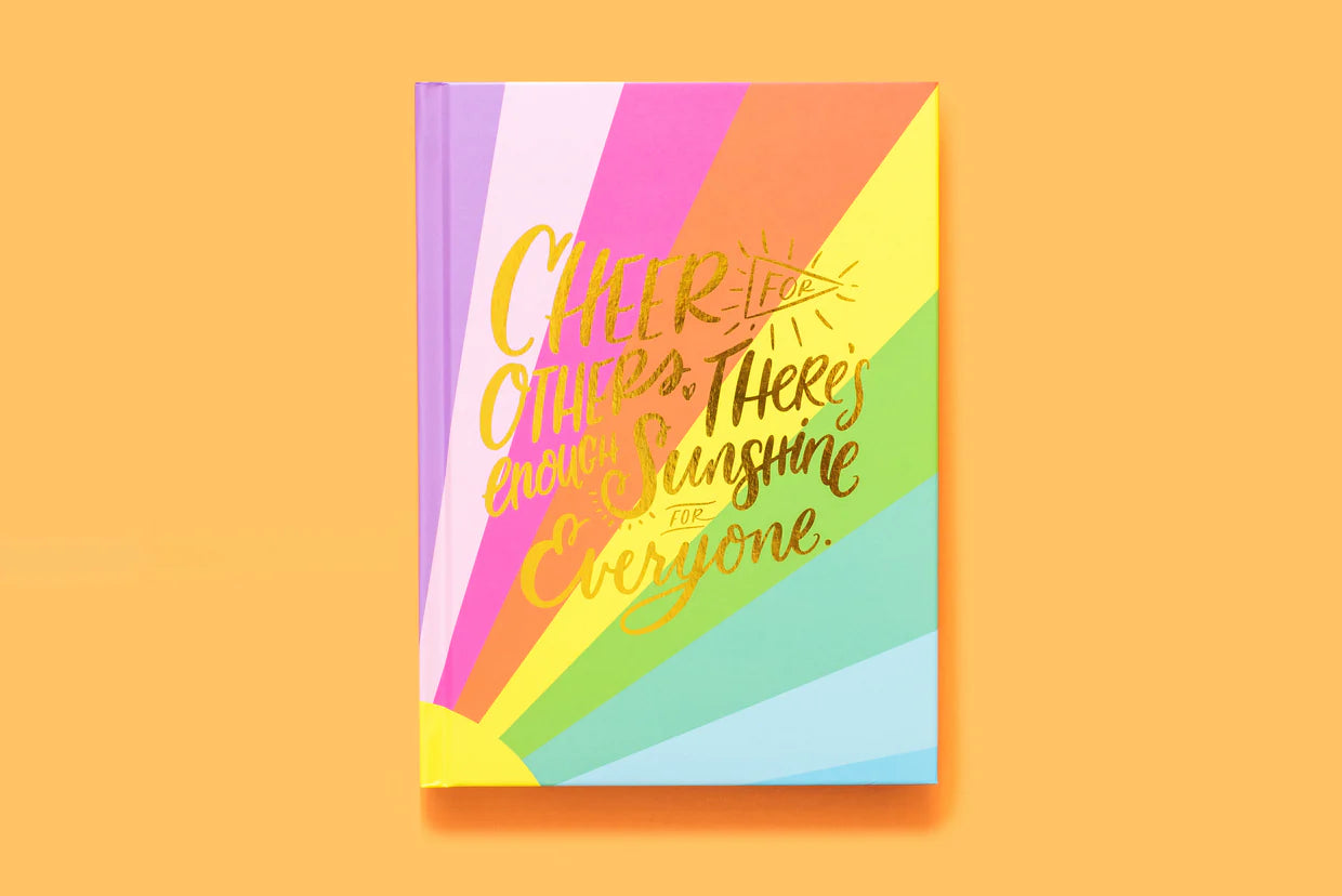 Colorful rainbow notebook with gold foil text on cover, inspirational stationery on orange background