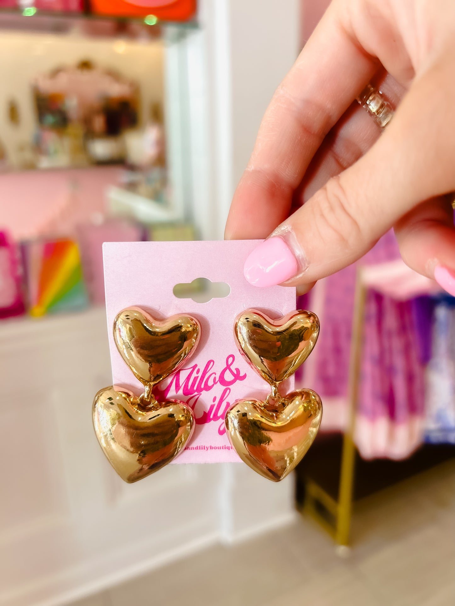 Hand holding gold heart dangle earrings with pink display card in boutique setting
