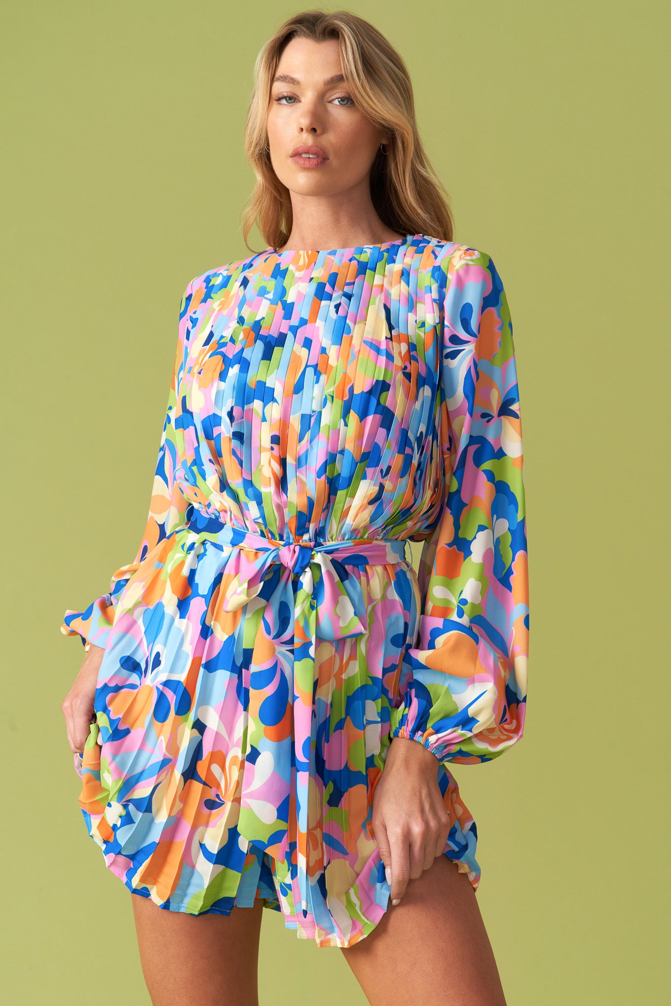 Vibrant floral pleated long sleeve romper with waist tie belt, featuring a bold multicolor print in blue, pink, orange, and green. Flowy, lightweight fabric with a flattering cinched waist, balloon sleeves, and an elegant round neckline. Perfect for stylish, playful fashion lovers at Milo & Lily Boutique.