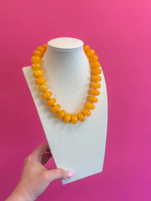 Orange beaded necklace on a white mannequin bust against a pink background