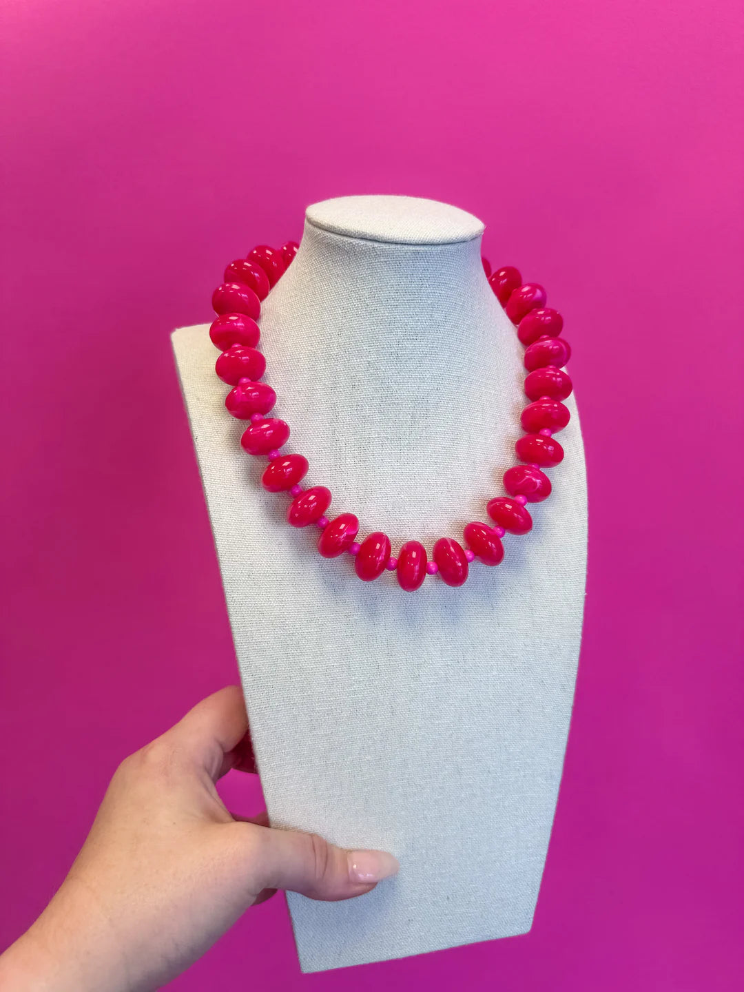 Pink beaded necklace on a mannequin bust against a pink background