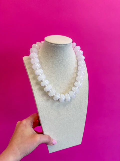 White beaded necklace on a mannequin bust against a pink background