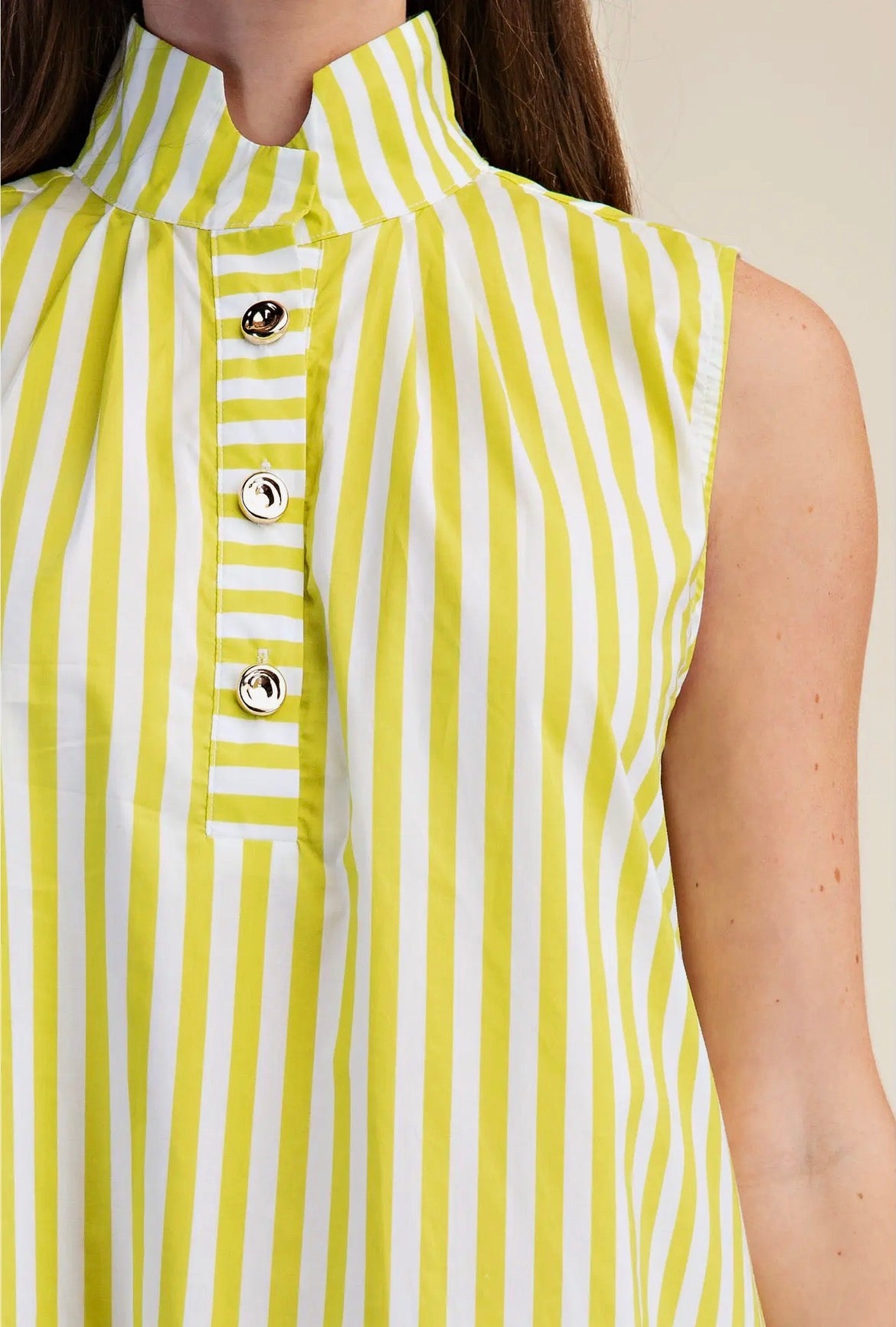 Close-up of a sleeveless high-neck top with vertical yellow and white stripes, featuring a buttoned placket and metallic buttons, worn by a model.