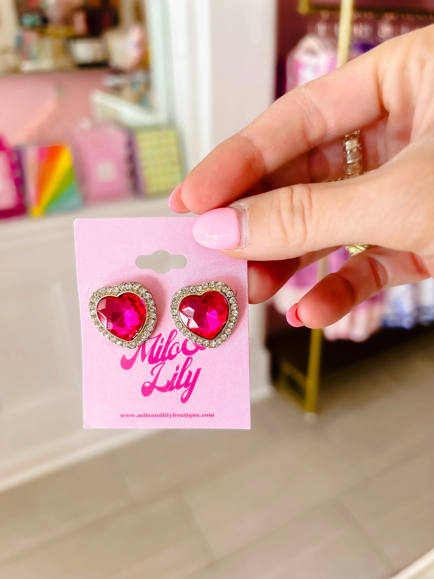 Hand holding pink jeweled heart earrings with rhinestone trim, women's fashion accessory