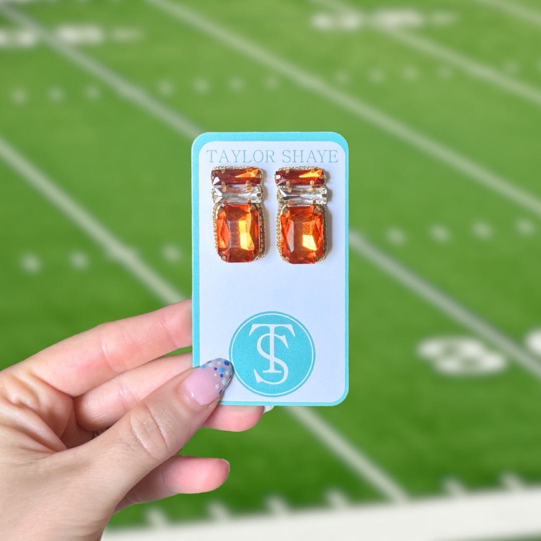 Hand holding a card with orange earrings against a football field background
