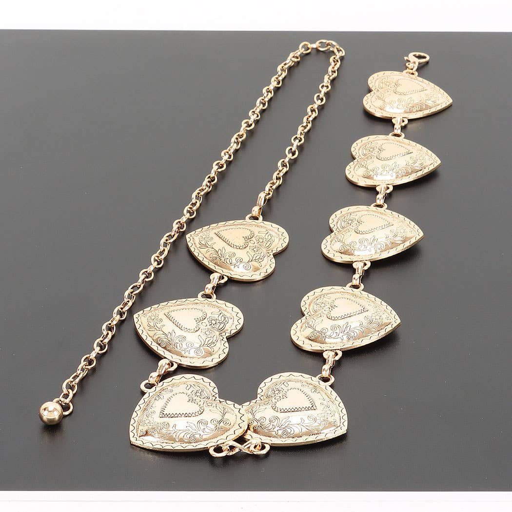 A gold-toned chain necklace featuring multiple textured, heart-shaped pendant links with engraved floral details, displayed on a dark gray background.