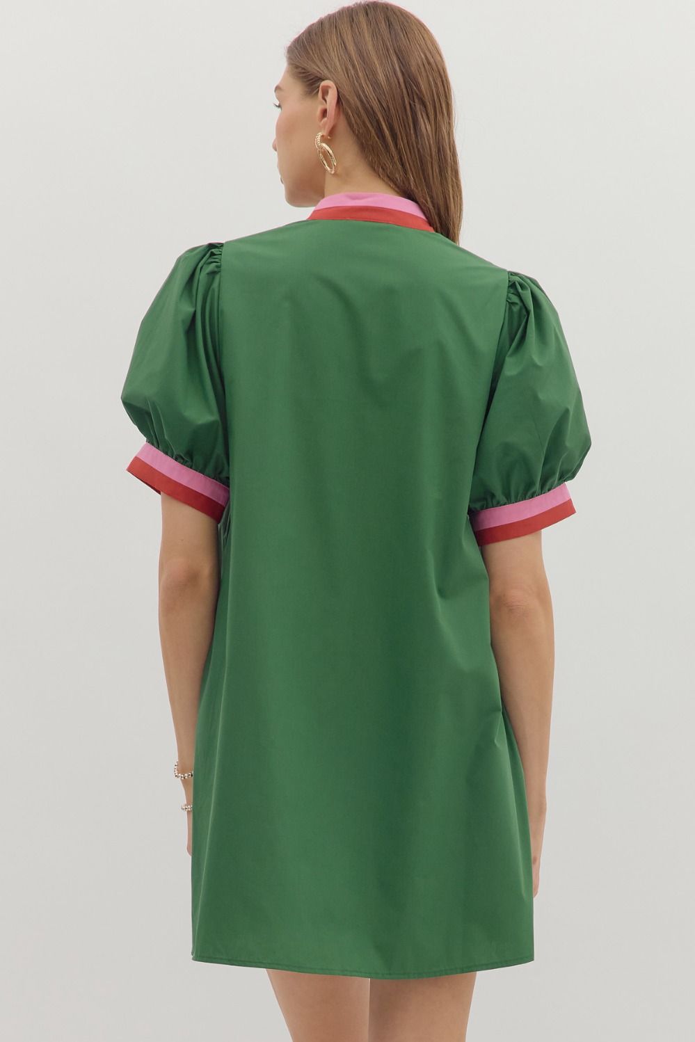 Back view of green mini dress with puff sleeves and pink and red striped cuffs; solid color design with a straight hemline.