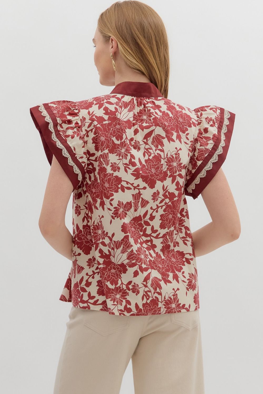Back view of a floral print blouse featuring ruffle-trimmed flutter sleeves and a relaxed fit, styled with neutral pants.
