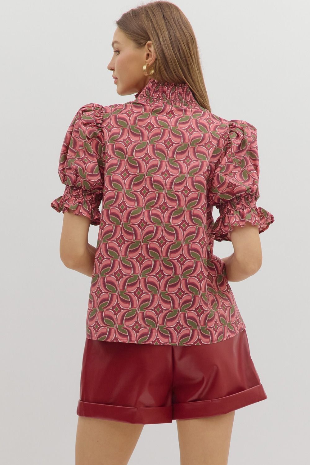 Back view of pink and olive geometric print puff sleeve blouse with shirred mock neck and smocked cuffs, paired with burgundy leather shorts – Milo & Lily Boutique.