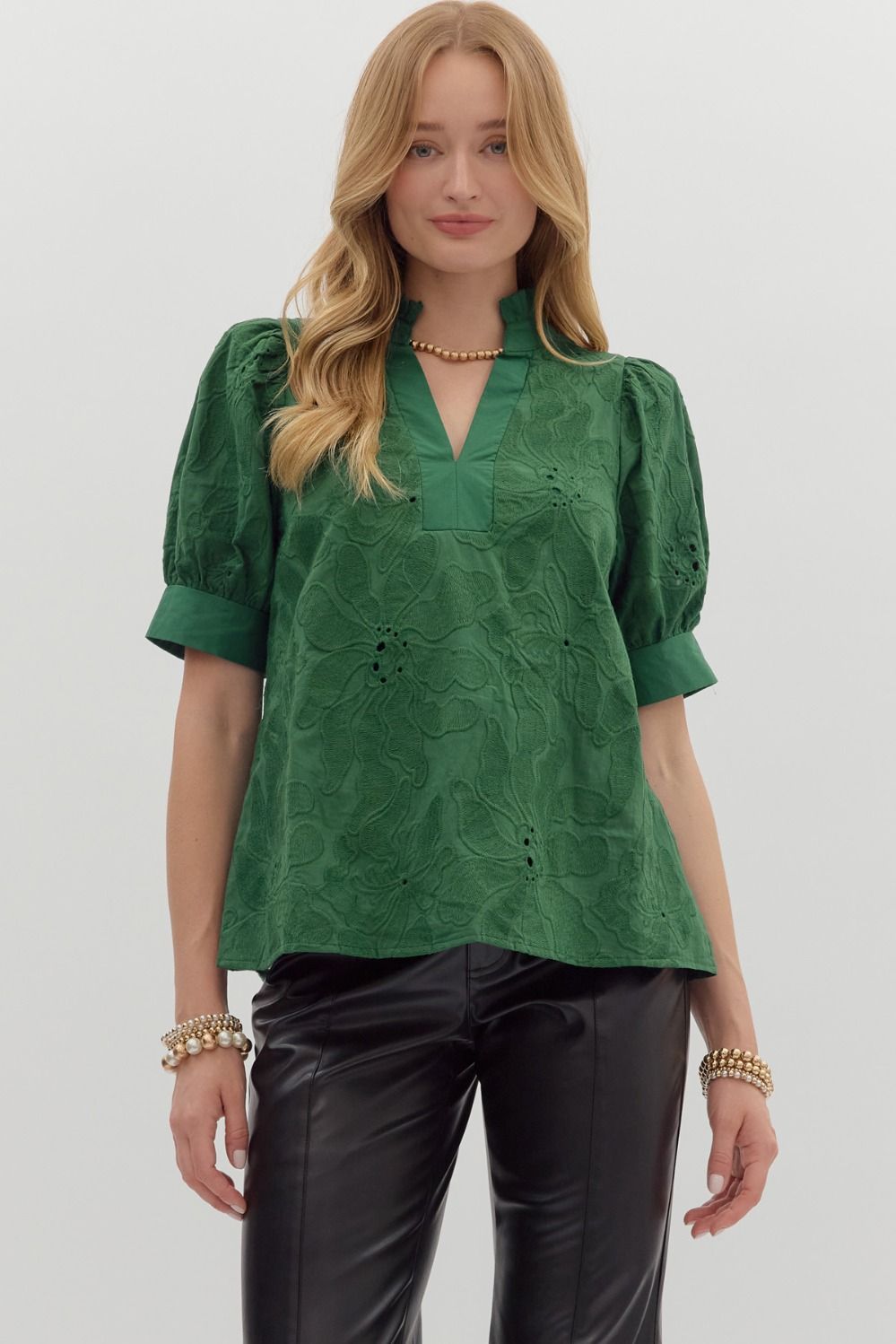 Woman wearing the Emerald Bloom Eyelet Top, a puff sleeve green blouse with floral eyelet embroidery, split neckline, and cuffed sleeves, paired with black leather pants – Milo & Lily Boutique.