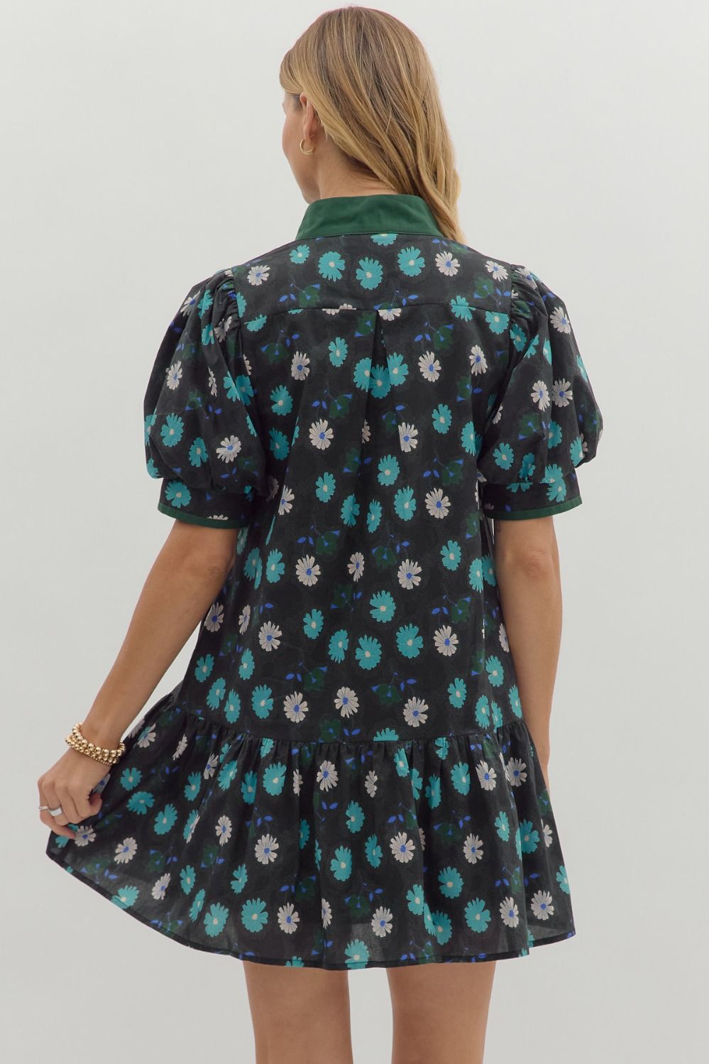 Woman wearing short black floral dress with puff sleeves and green collar, back view