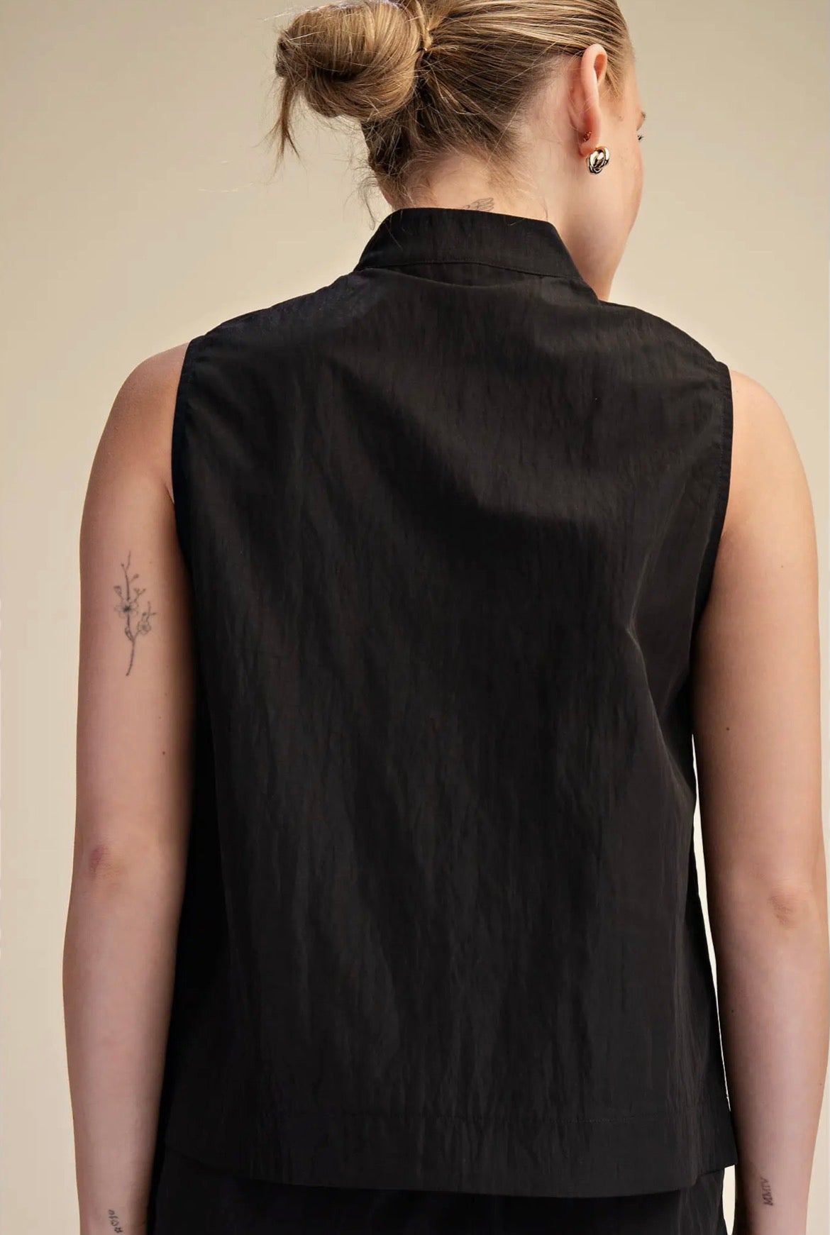 A woman shown from the back wearing a sleeveless black vest against a plain beige studio background.