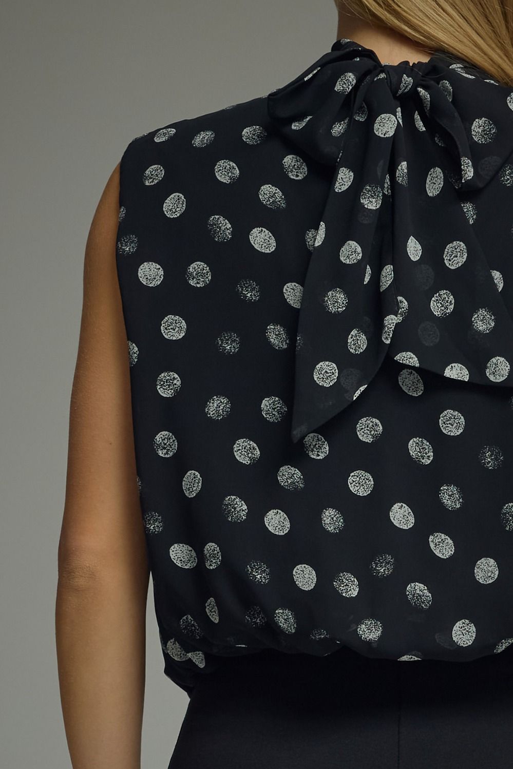 Black sleeveless top with silver polka dots and a bow detail on a gray background