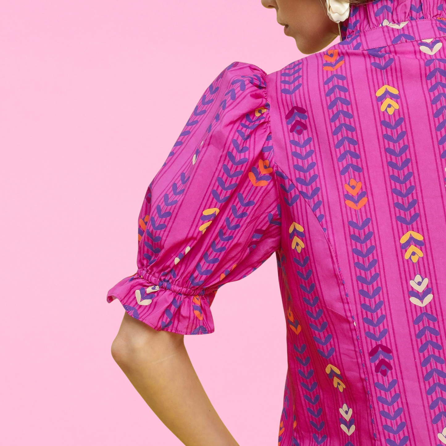 Close-up of a woman wearing a bright magenta blouse with puff sleeves and colorful geometric embroidery, showing ruffle cuff and back collar details.
