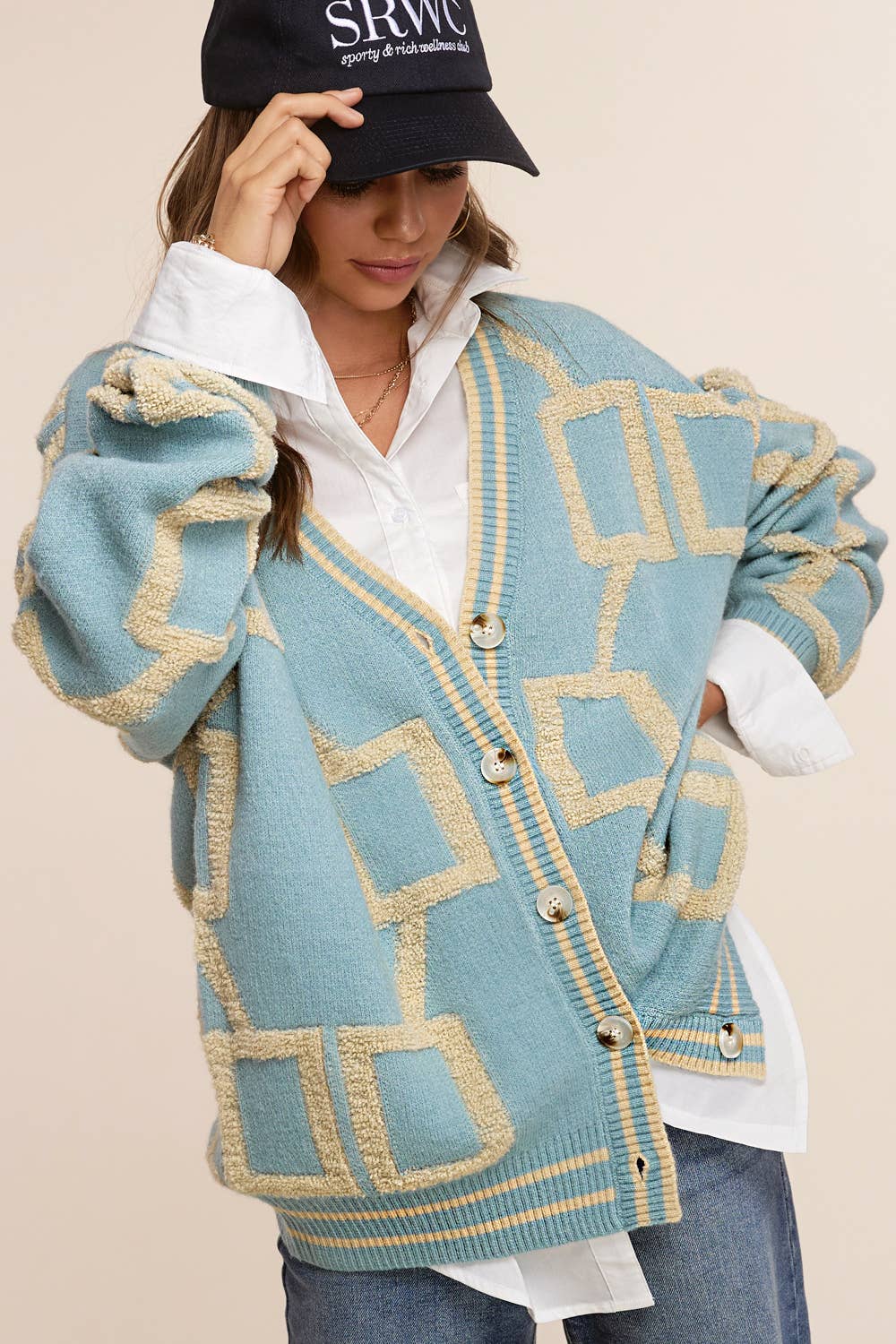 Woman wearing a blue patterned cardigan over a white shirt with a black cap.