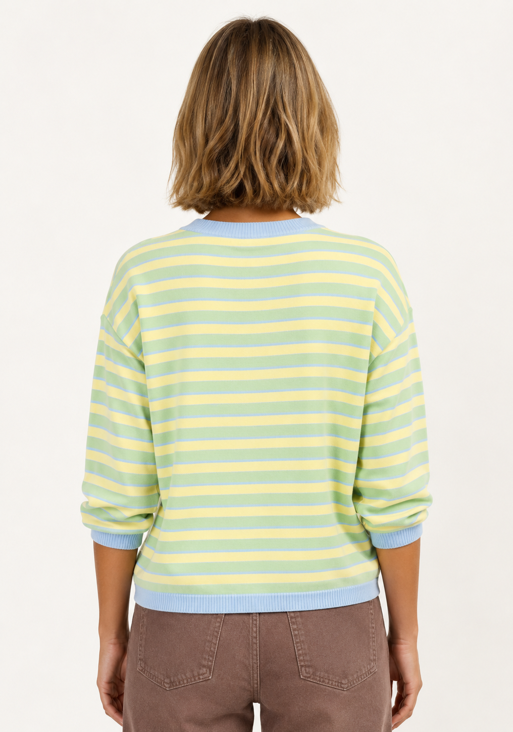 A woman viewed from behind wearing a pastel striped knit sweater with light blue and pale yellow horizontal stripes, paired with brown pants, against a plain white background.