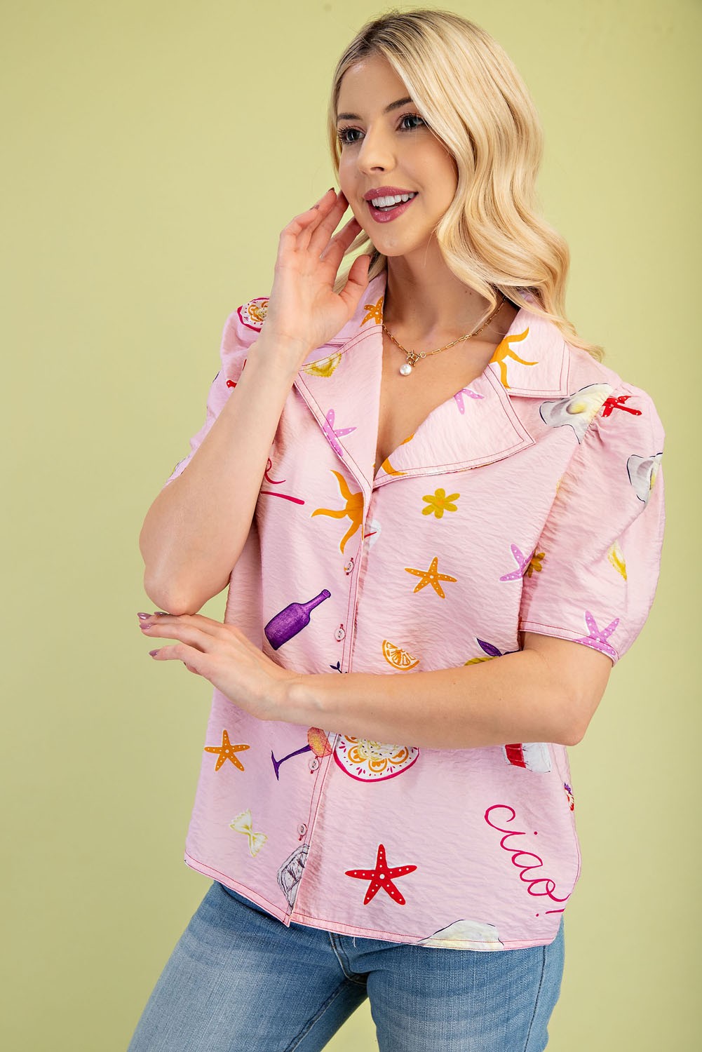 Woman wearing a pink short-sleeve collar shirt with colorful vacation-themed prints and jeans