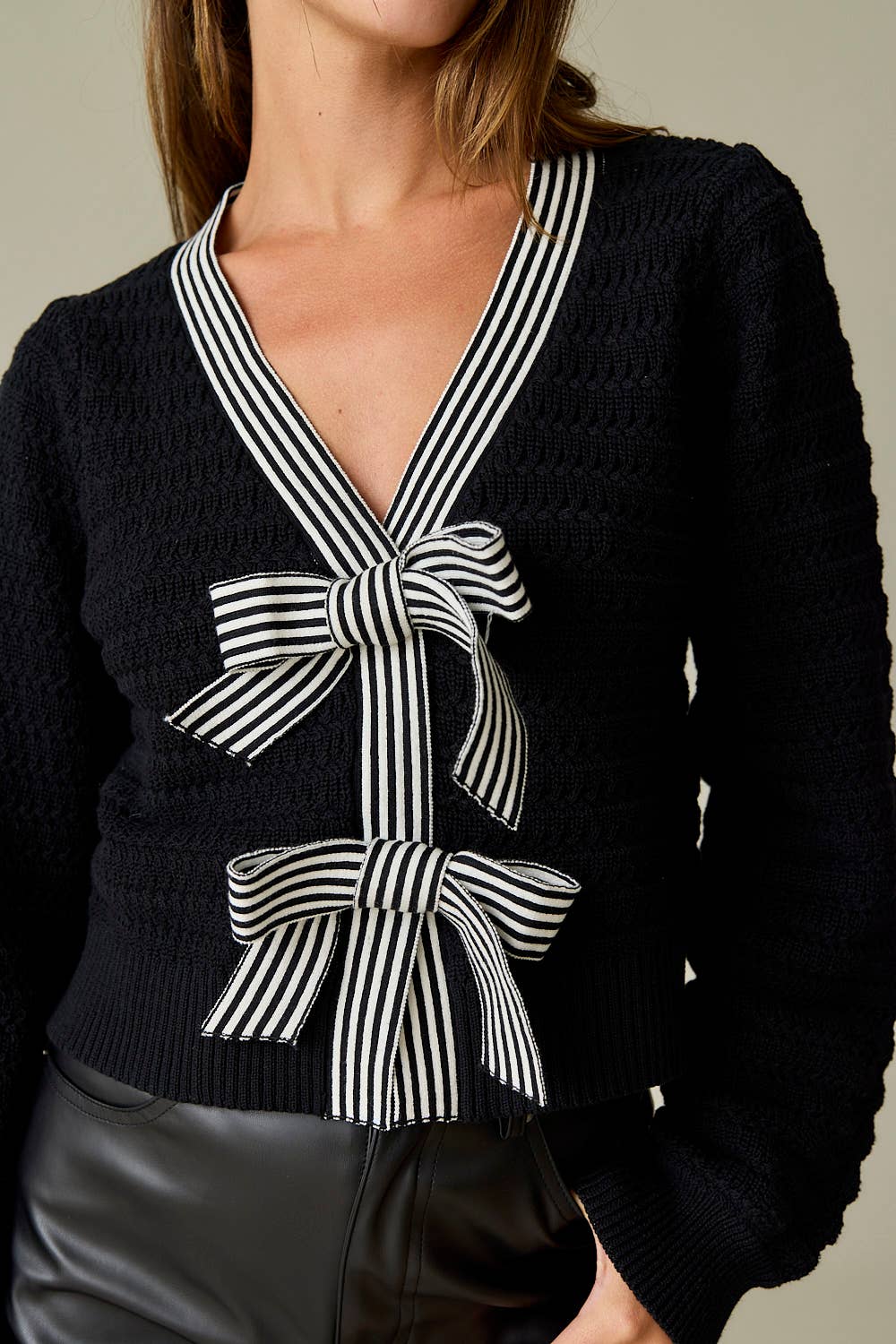 Close up of Black textured knit sweater with two black-and-white striped statement bows on the front and a deep V-neckline, styled with black leather shorts