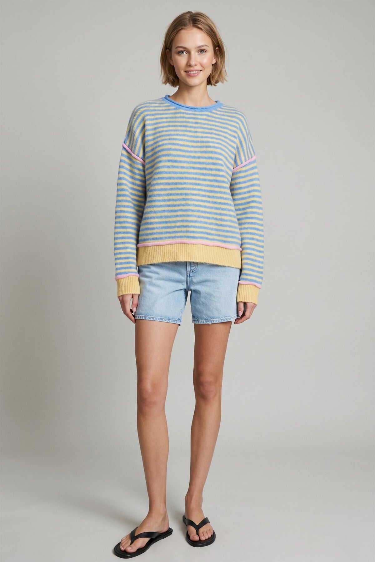 Model wearing blue and yellow striped relaxed sweater with light wash denim shorts.