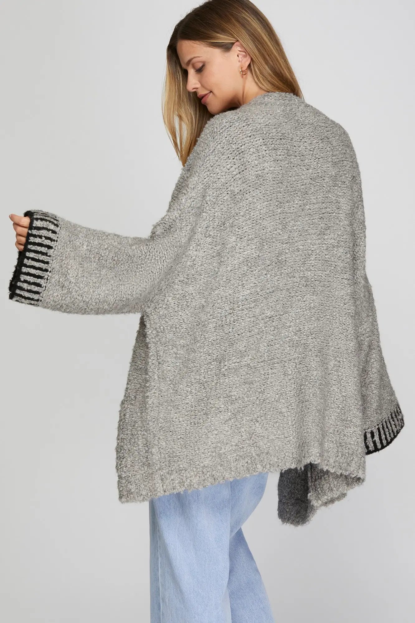 Woman wearing a gray cardigan with black fringe details on a white background