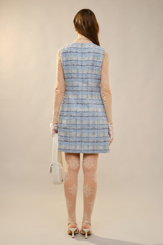 Woman wearing a blue and white patterned dress with sheer sleeves and holding a white handbag.