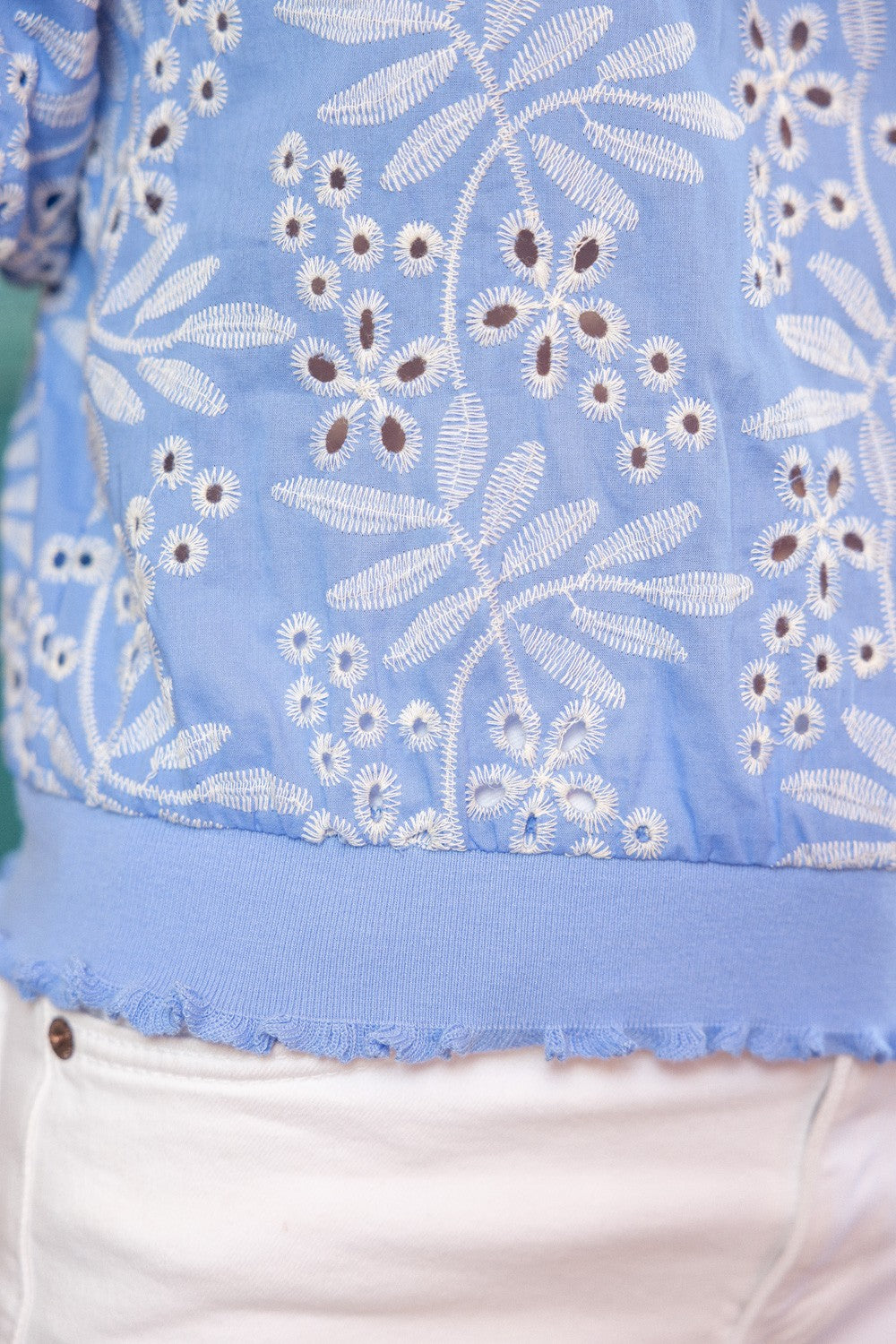 Close-up of blue embroidered eyelet top with ribbed hem and frilly ruffle trim.