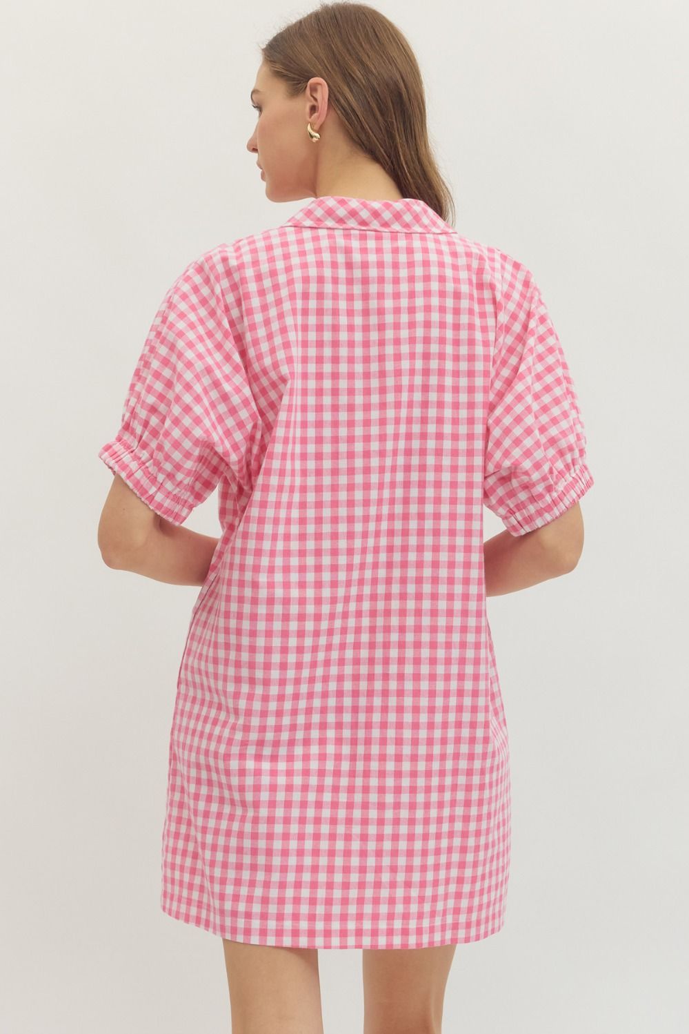 Woman wearing a pink and white checkered dress against a plain background