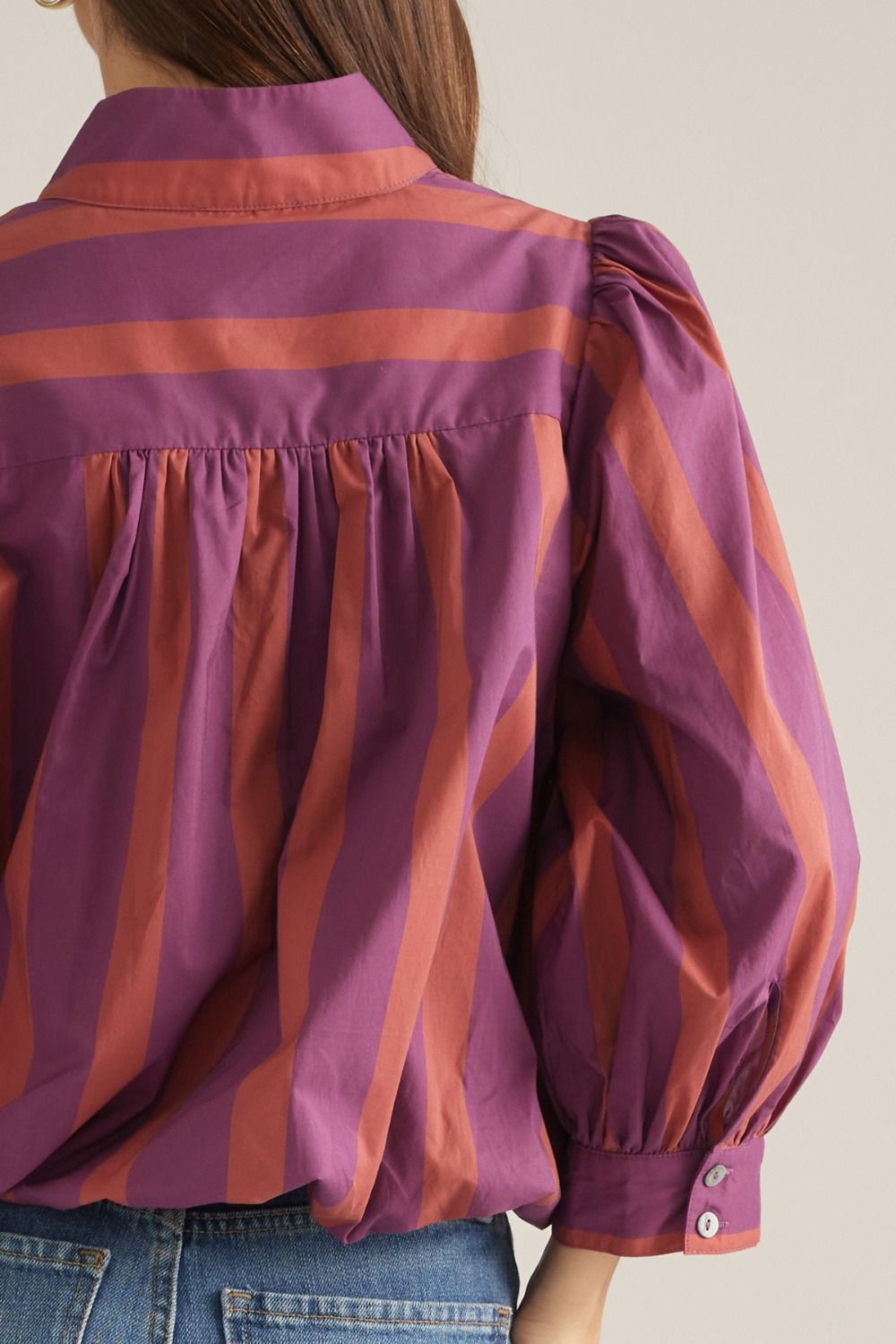 Close-up of gathered back yoke and buttoned sleeve cuff on plum and rust striped blouse.
