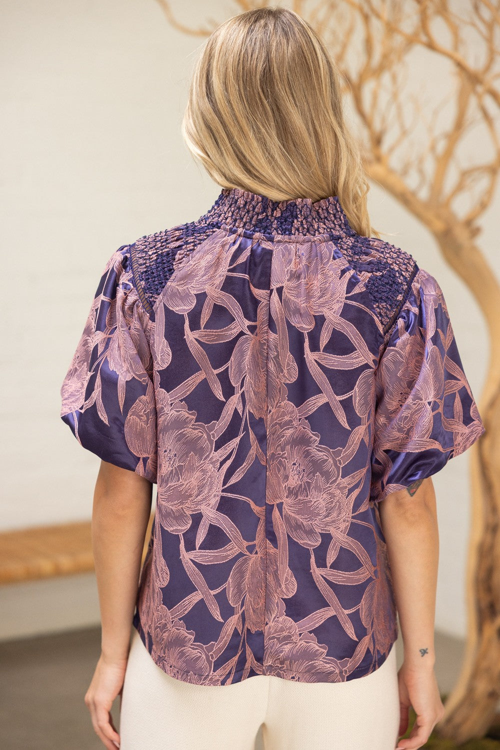 Back view of The Twilight Bloom Top highlighting smocked shoulders and blush floral print on violet satin fabric