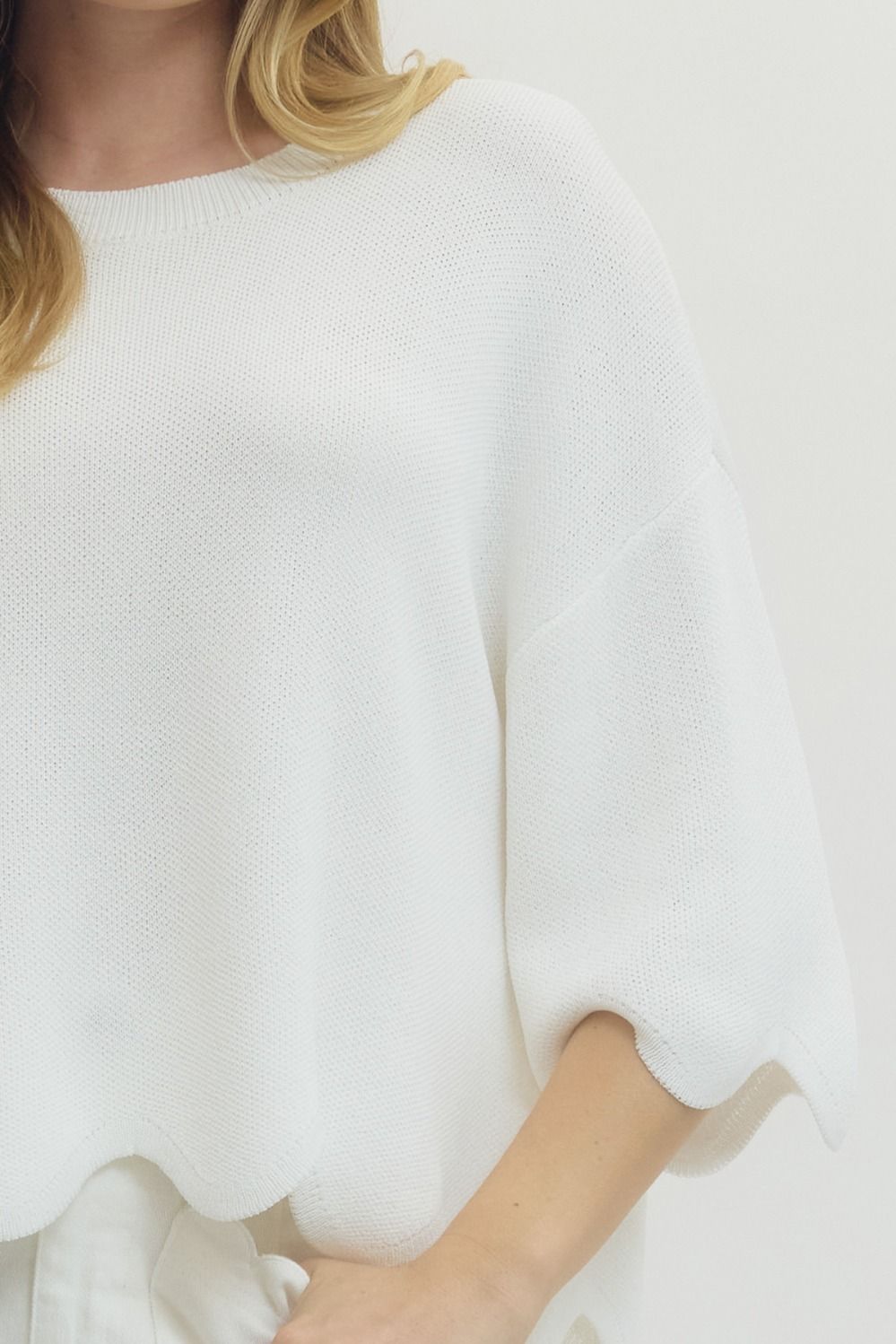 Detail view of white scalloped hem knit sweater top with soft textured fabric