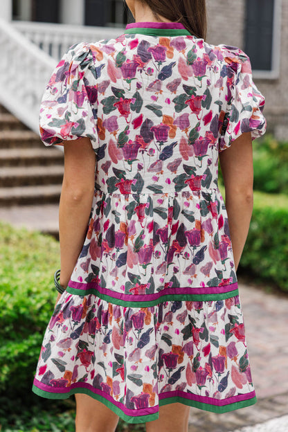 Back view of woman wearing short puff sleeve floral dress with pink and green trim outdoors