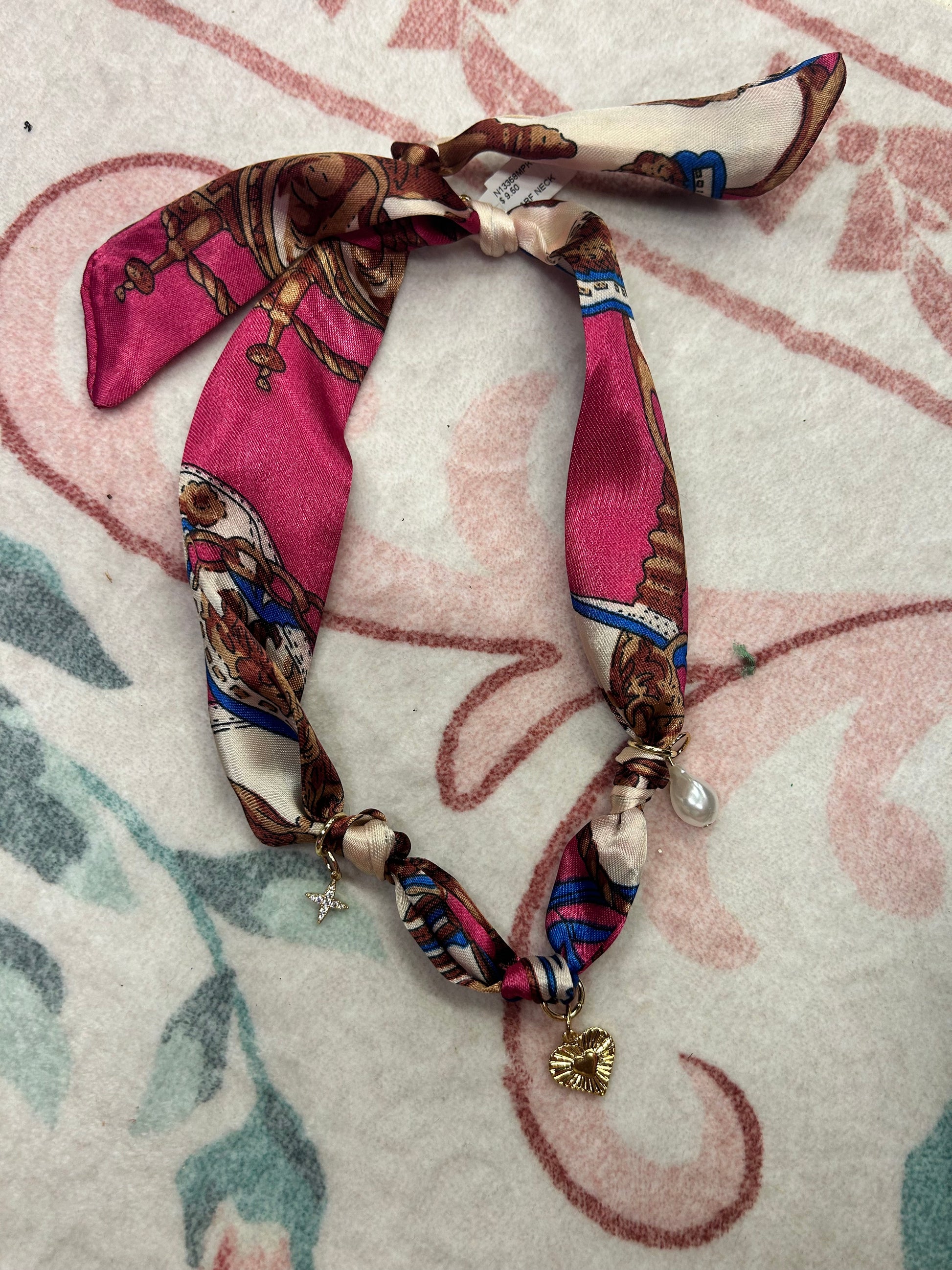 Patterned pink silk scarf necklace with gold heart, star, and pearl charms on a floral background