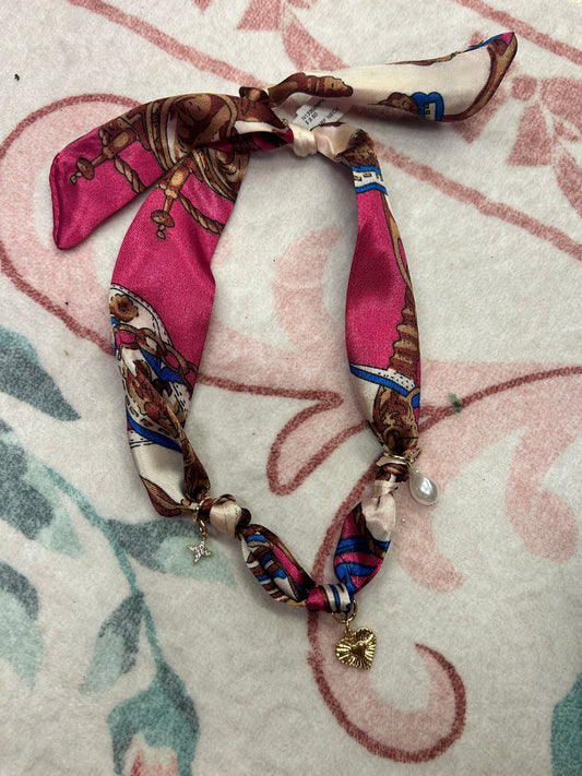 Patterned pink silk scarf necklace with gold heart, star, and pearl charms on a floral background