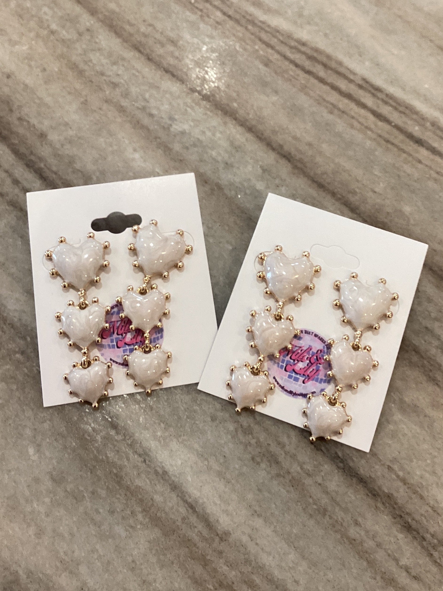 White heart stud earrings with gold accents on display cards, on a marble surface