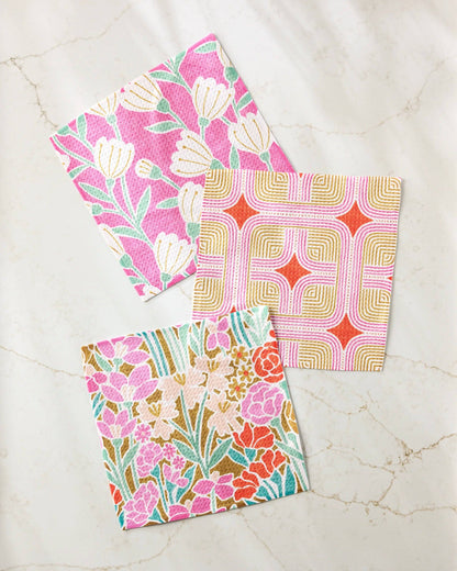 Three colorful floral and geometric patterned dishcloths on a marble surface