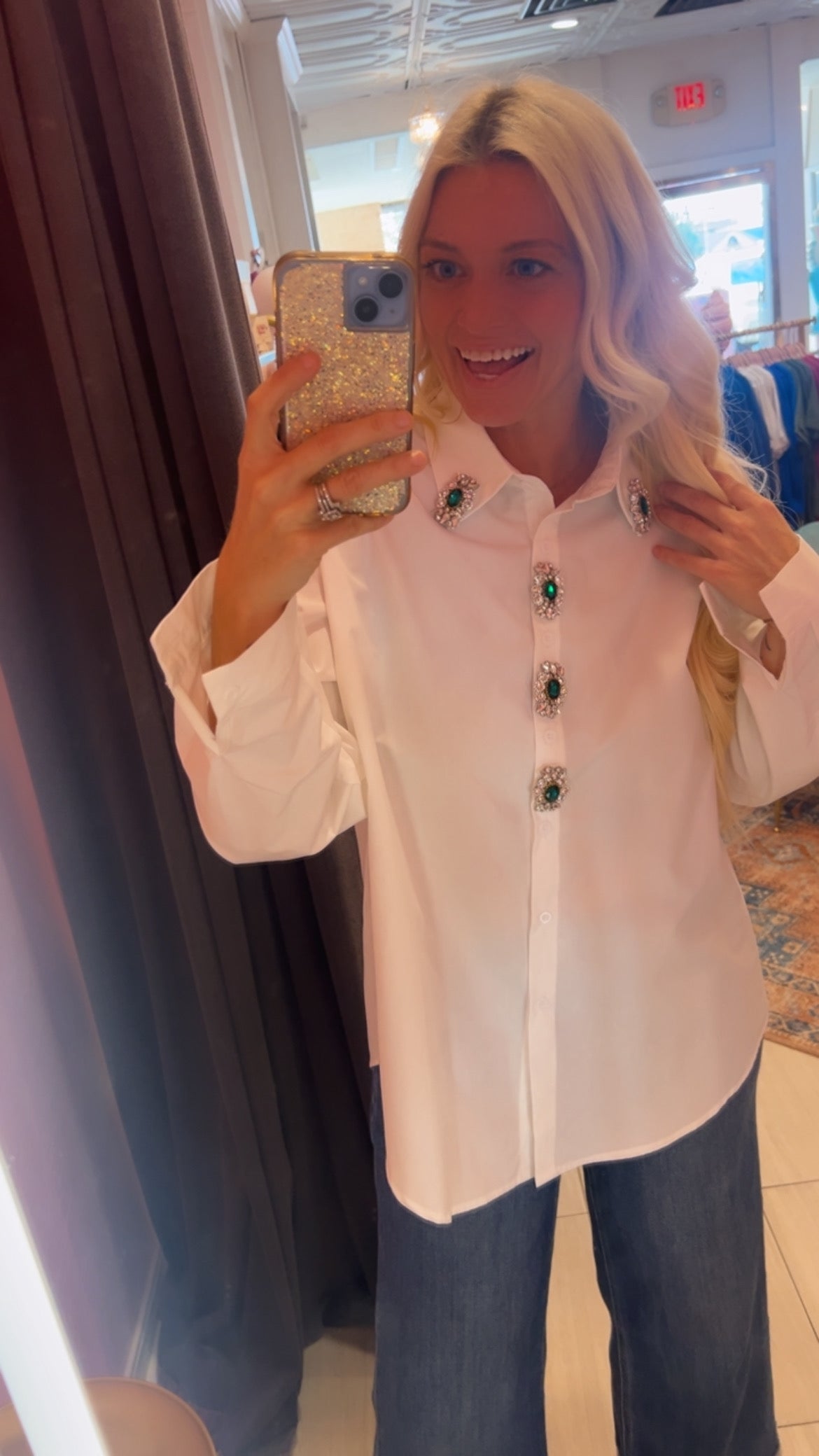 Woman wearing white blouse with jeweled emerald buttons and blue denim jeans