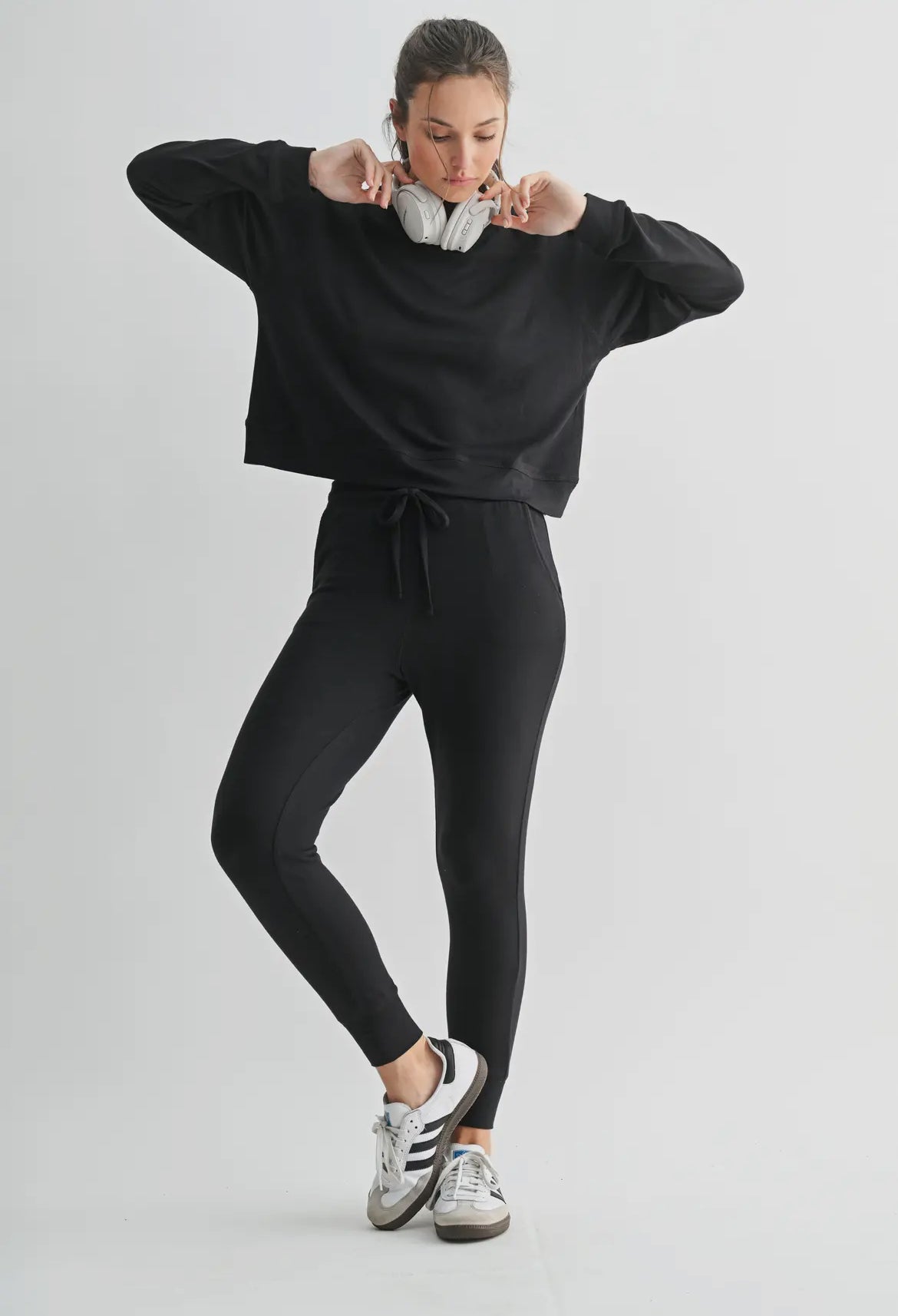 Woman wearing black lounge set with joggers, black sneakers, and headphones.