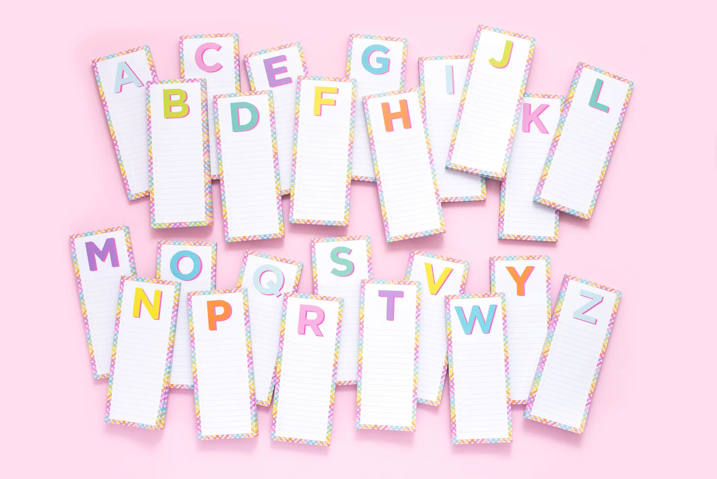 Colorful alphabet notepads with lined paper on pink background, stationery for notes