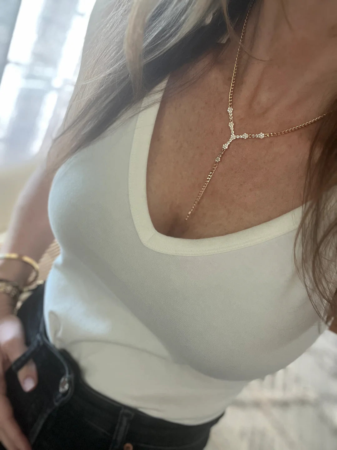 Woman wearing a white V-neck tank top, gold Y-shaped necklace, and black jeans
