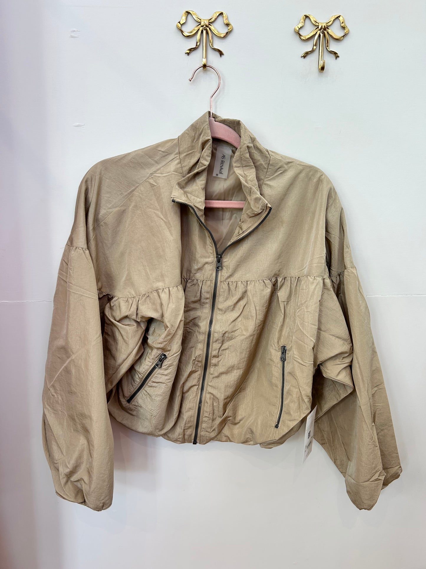 Beige zip-up cropped jacket with long sleeves and front pockets, hanging on wall hook
