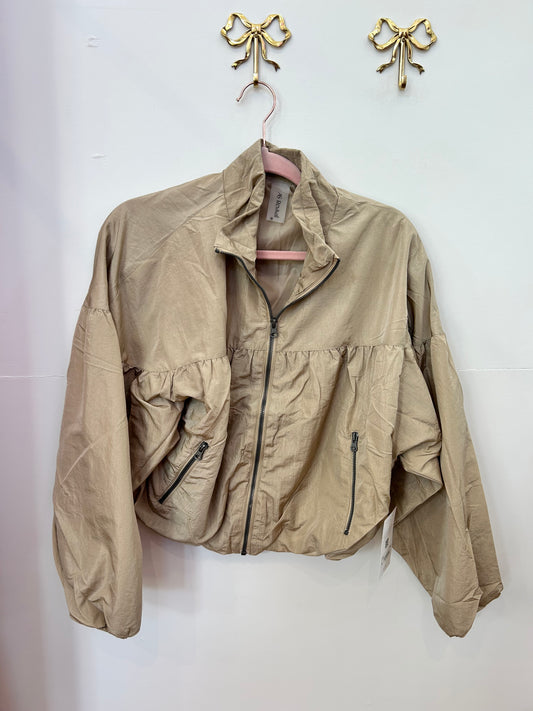 Beige zip-up cropped jacket with long sleeves and front pockets, hanging on wall hook