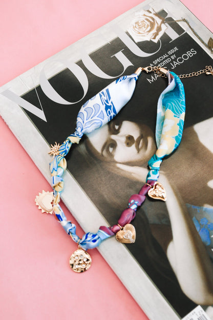 Colorful silk and gold charm necklace with heart and sun pendants on a fashion magazine