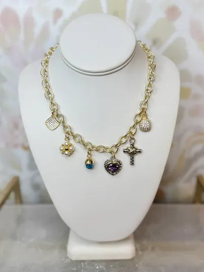 Gold charm necklace with heart, cross, and gemstone pendants on a display bust.