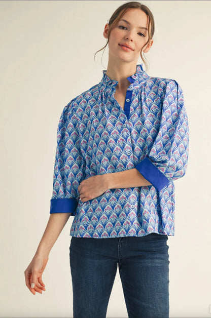 Woman wearing a blue patterned blouse with ruffled collar and blue cuffed sleeves, paired with jeans