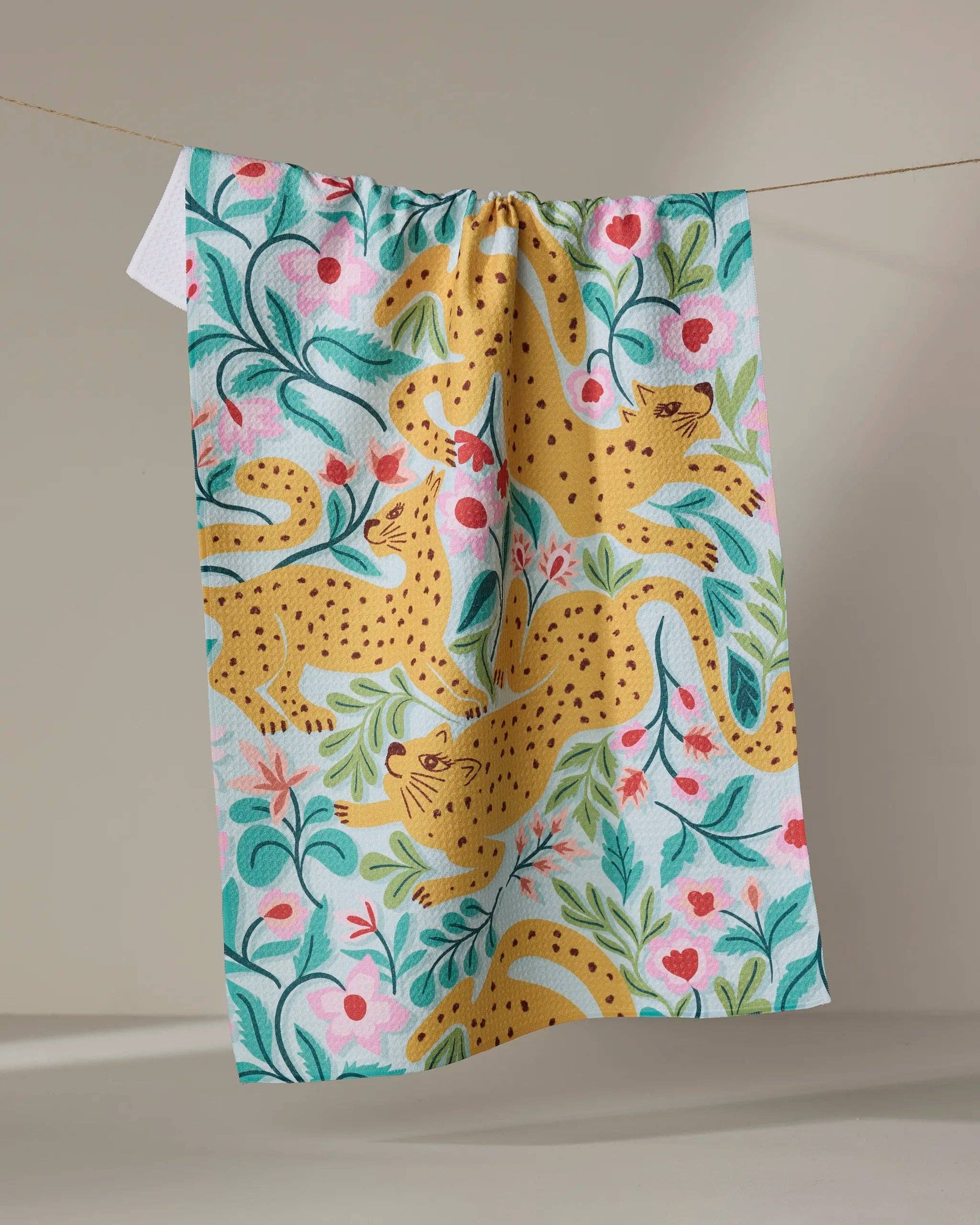 Colorful tea towel with yellow leopard and floral print hanging on a line