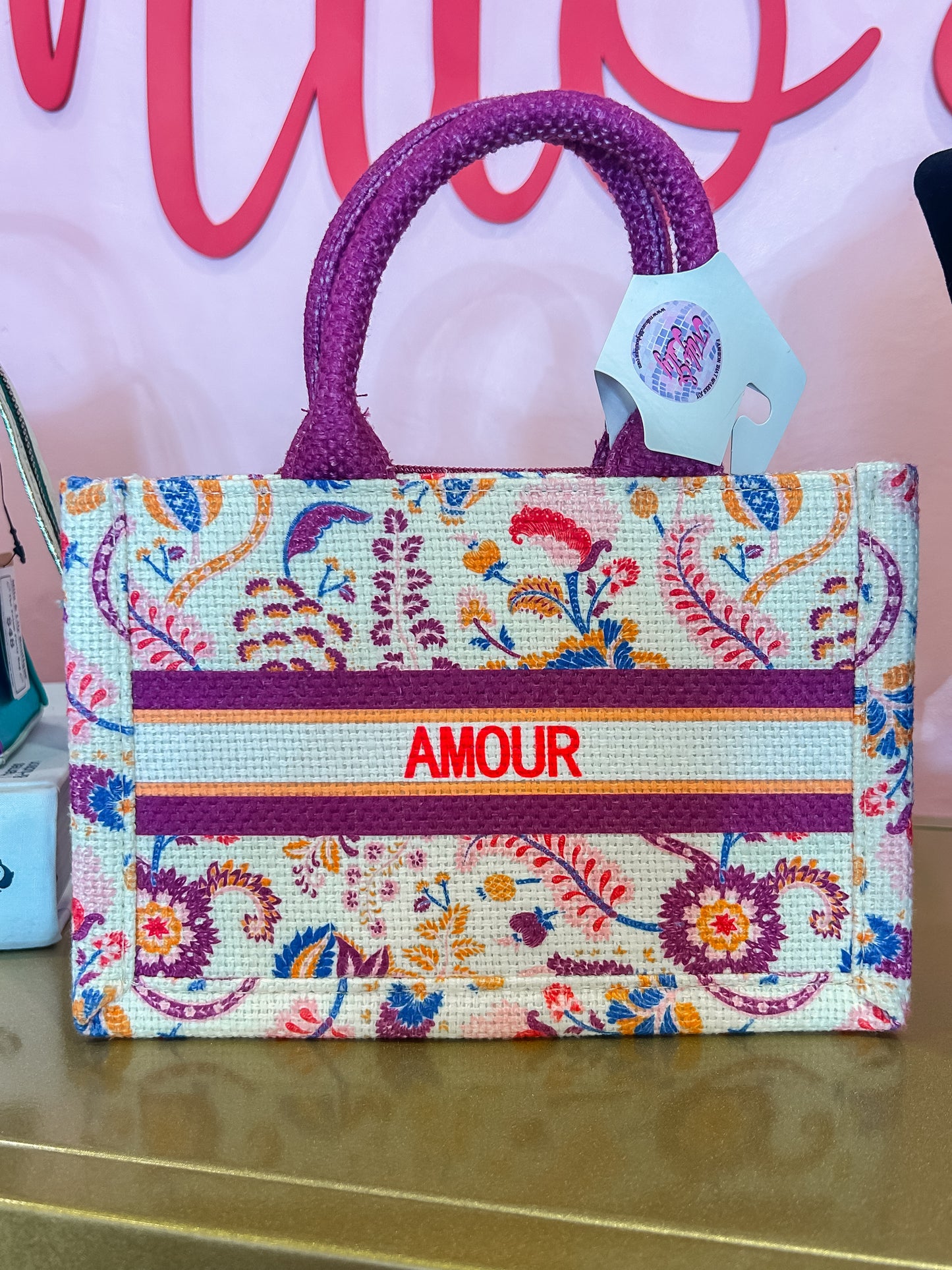 Floral woven handbag with purple handles and 'AMOUR' text, boutique display